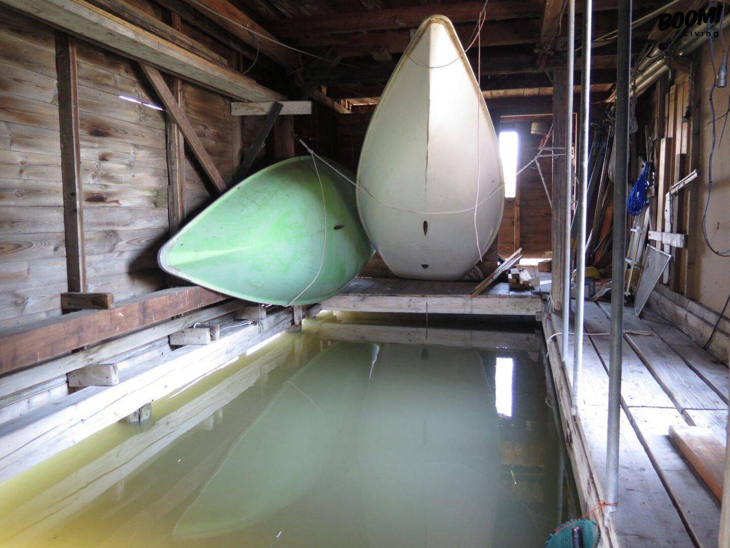 Innenansicht eines Bootshauses mit zwei Booten und direktem Wasserzugang, umgeben von Holzkonstruktion.