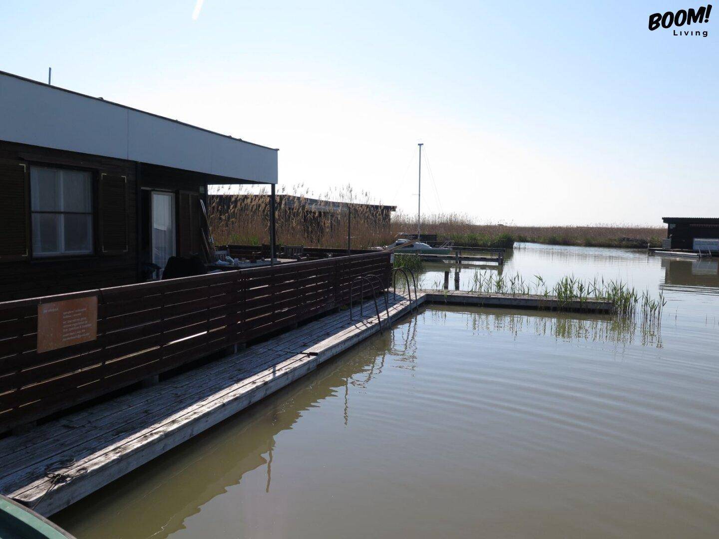 Hausboot am Wasser mit Holzfassade und einem Holzsteg für den einfachen Zugang zum Boot.