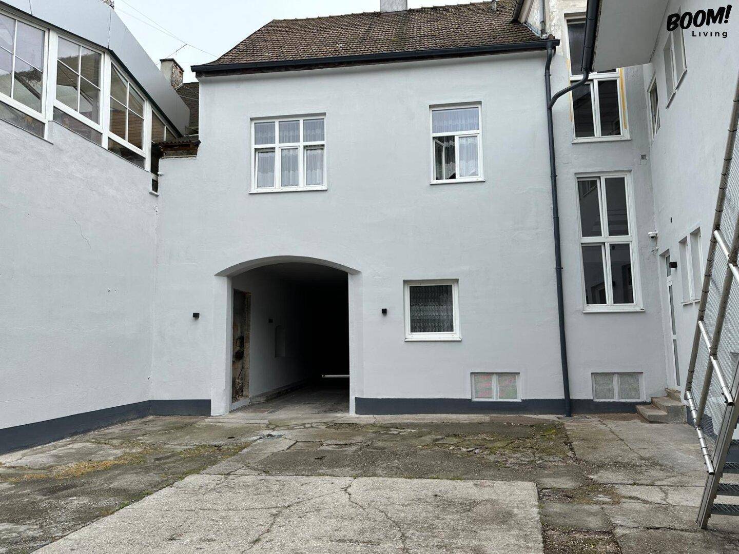 Innenhof mit Durchfahrt und hellgrauer Fassade eines älteren Gebäudes.