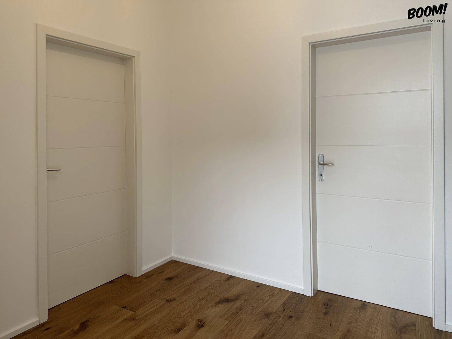 Heller Raum mit zwei modernen weißen Türen und einem Holzboden.