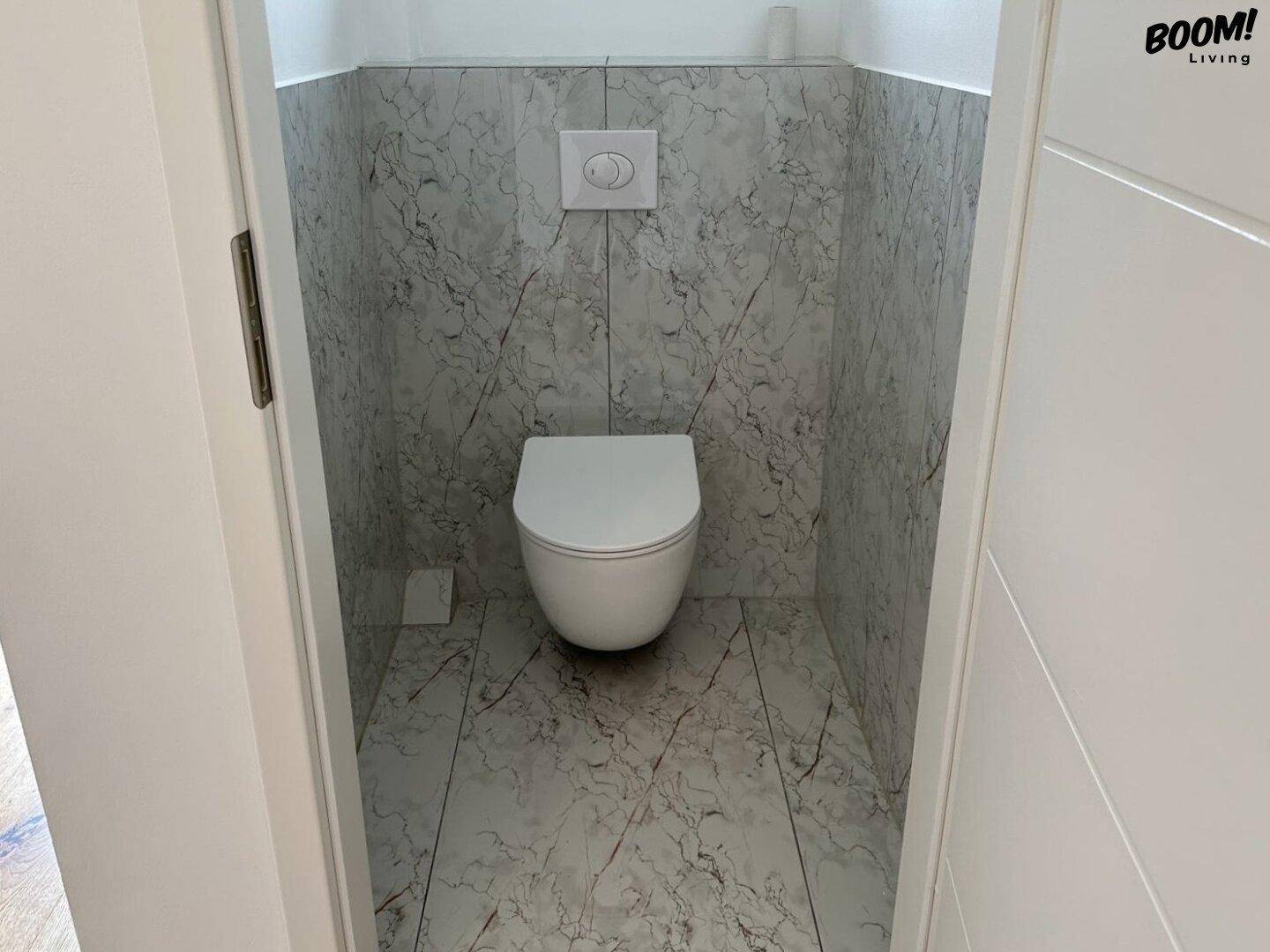 Modernes Gäste-WC mit wandhängender Toilette und hellgrauen Marmorfliesen.