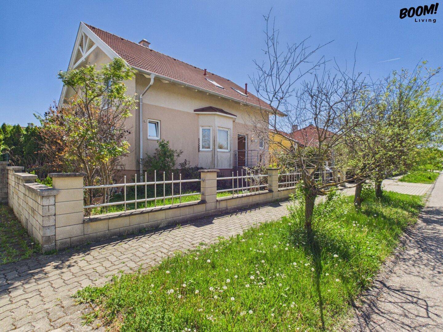 Seitenansicht des Hauses mit Vorgarten, Zaun und gepflastertem Gehweg unter blauem Himmel.