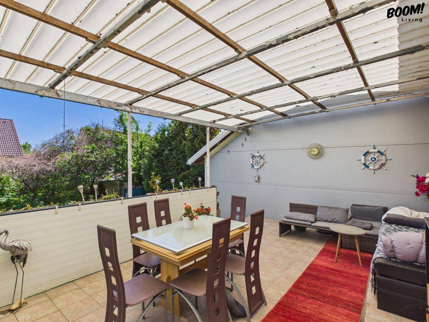 Überdachte Terrasse mit Esstisch, Sitzgelegenheiten und Blick ins Grüne.