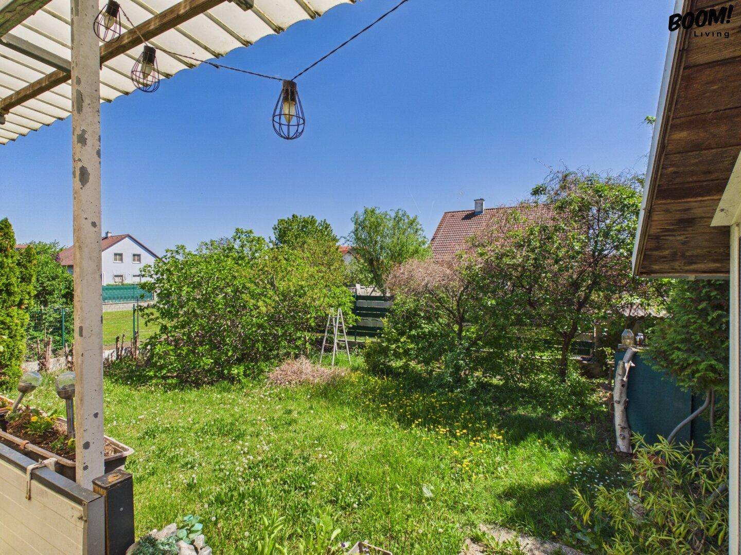 Blick von der Terrasse in den grünen Garten mit Rasenfläche und Bäumen.