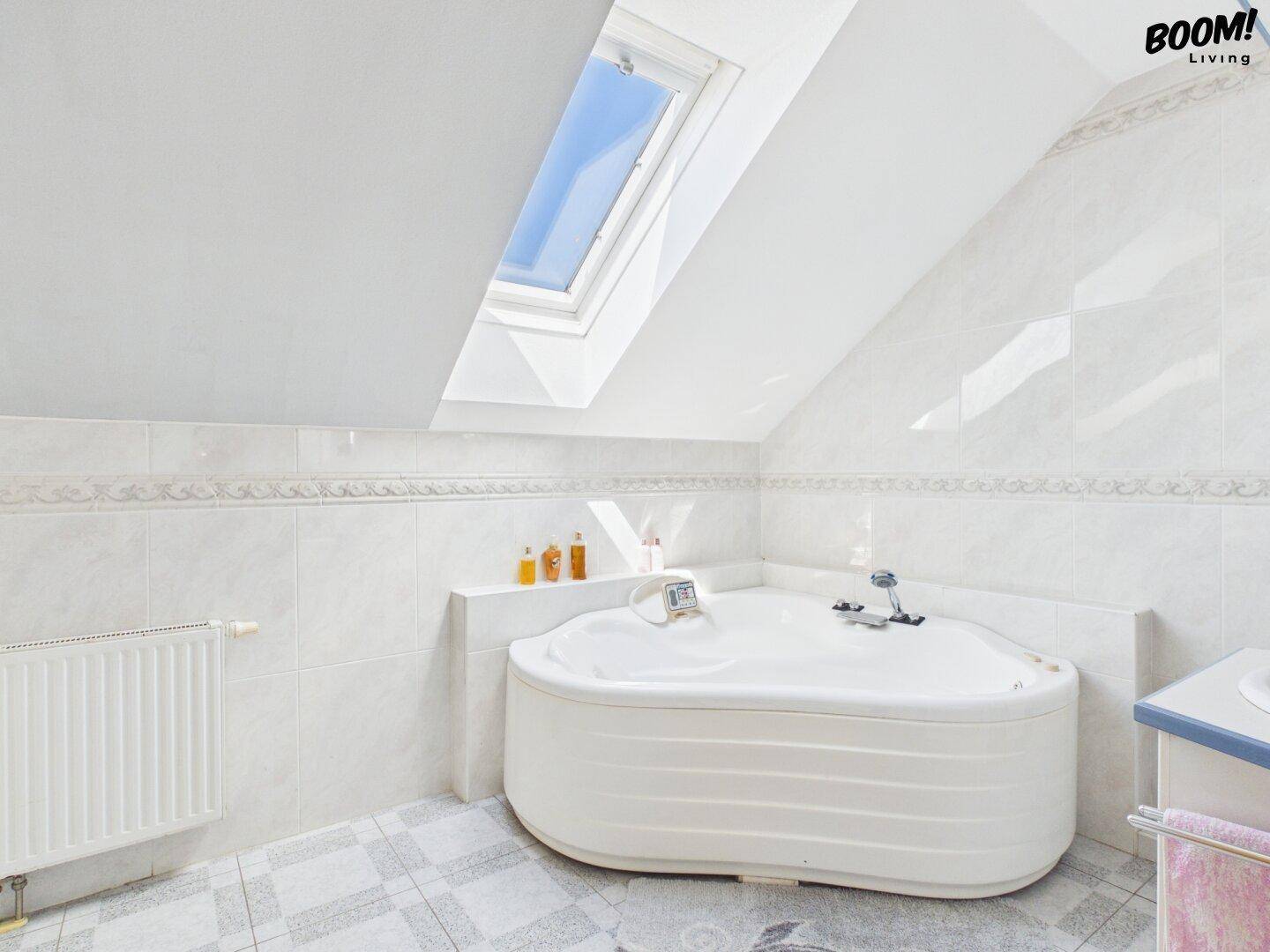 Helles Badezimmer mit Eckbadewanne, Fliesen und Dachfenster für natürliches Licht.