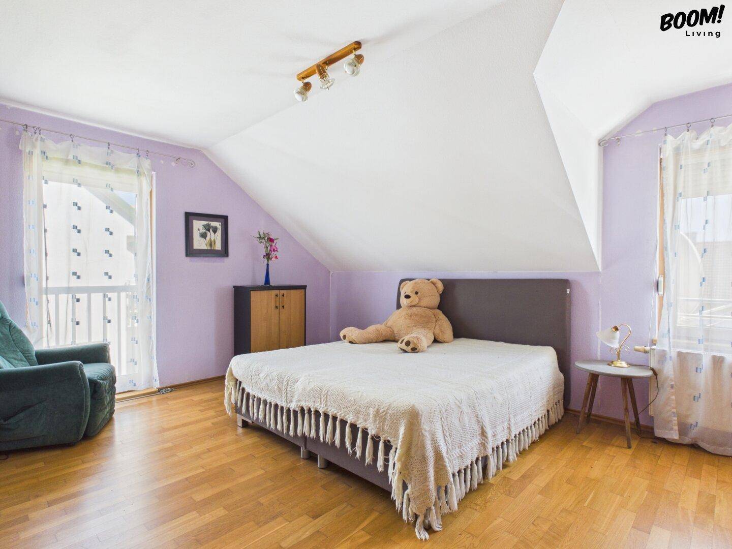 Gemütliches Schlafzimmer im Dachgeschoss mit lila Wänden, Parkettboden und Dachschräge.