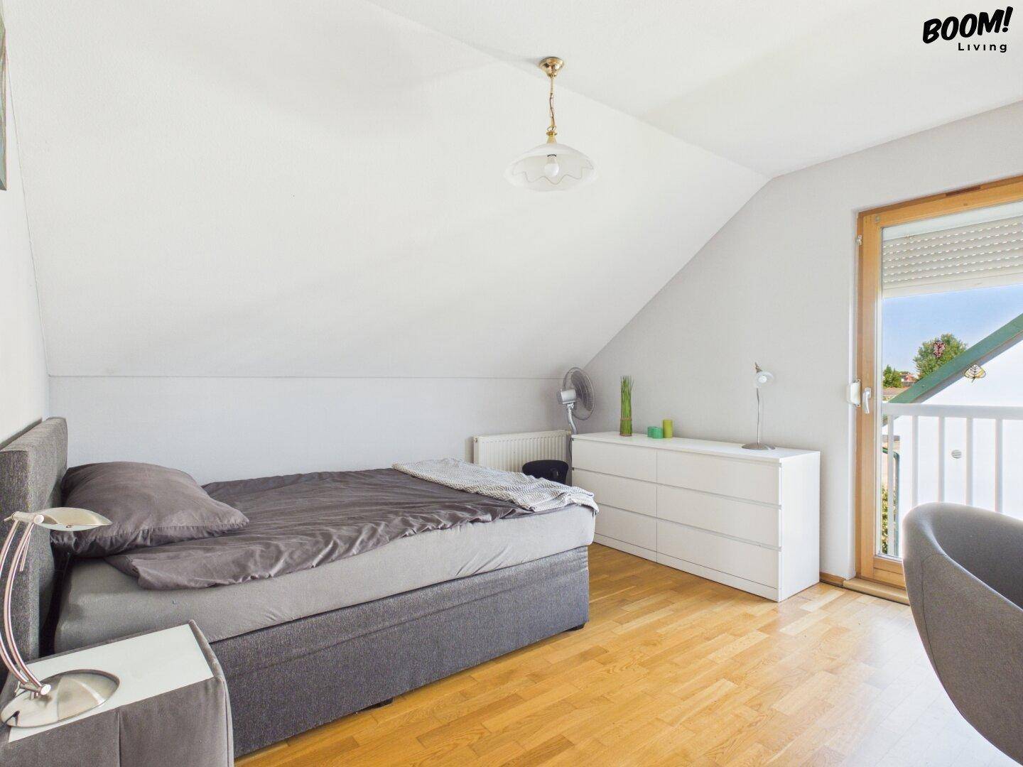Helles Schlafzimmer im Dachgeschoss mit Parkettboden, Dachschräge und Zugang zum Balkon.