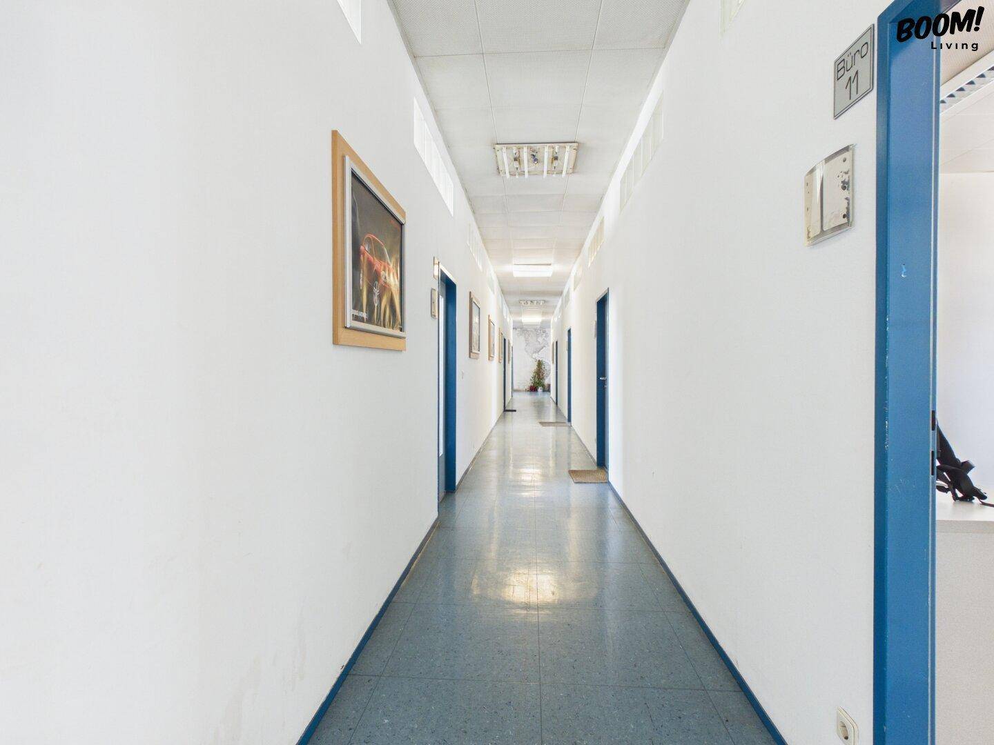 Langer, heller Flur mit blauen Türen und einem blauen Bodenbelag.