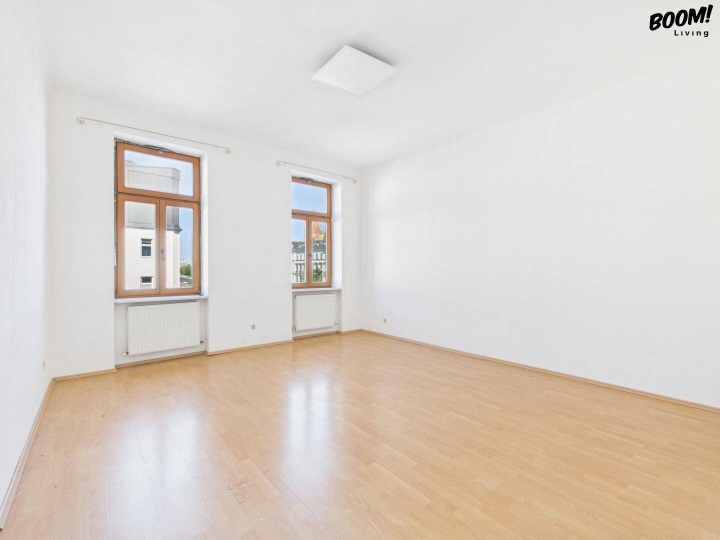 Leeres, helles Zimmer mit Parkettboden und zwei großen Fenstern, bereit zur individuellen Gestaltung.