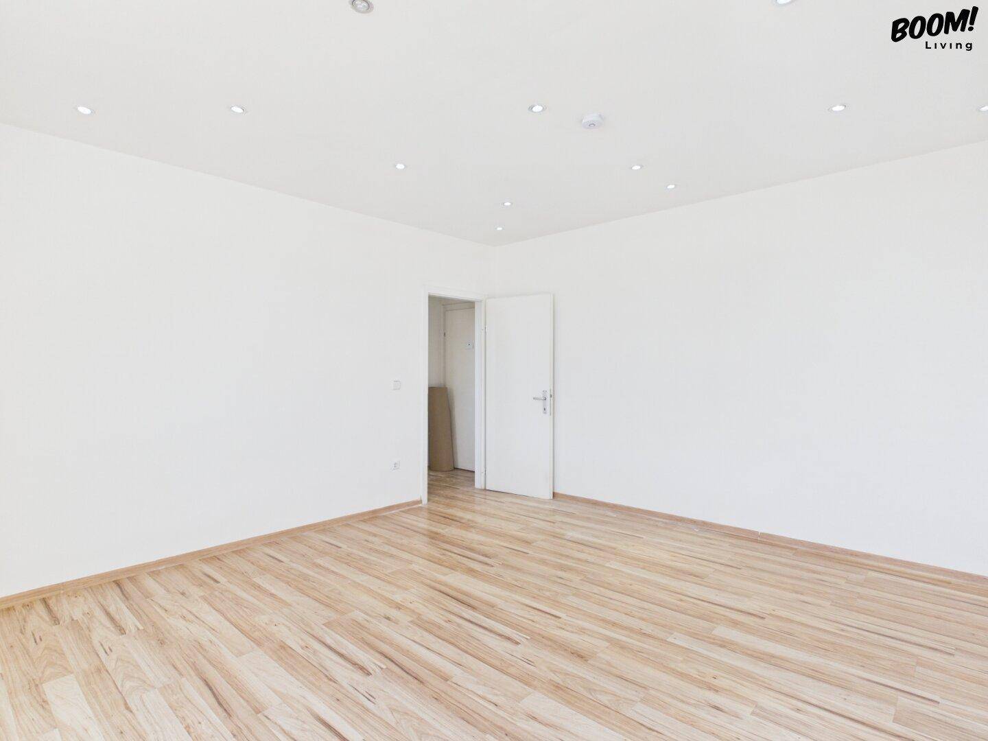 Geräumiger, heller Raum mit Holzparkettboden und moderner Deckenbeleuchtung.