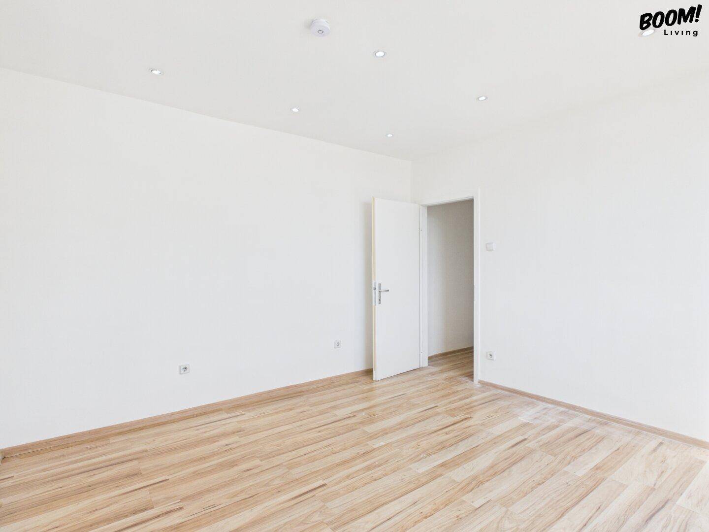 Heller, leerer Raum mit Holzparkettboden und weiß gestrichenen Wänden.
