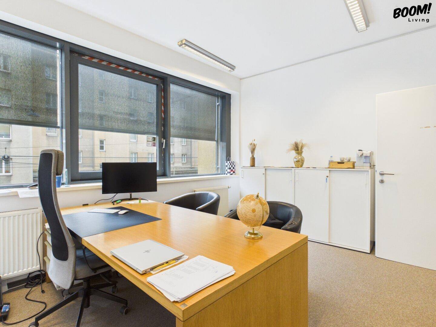 Modernes Büro mit Holzschreibtisch, Bürostühlen und Schränken, gut beleuchtet durch große Fenster.