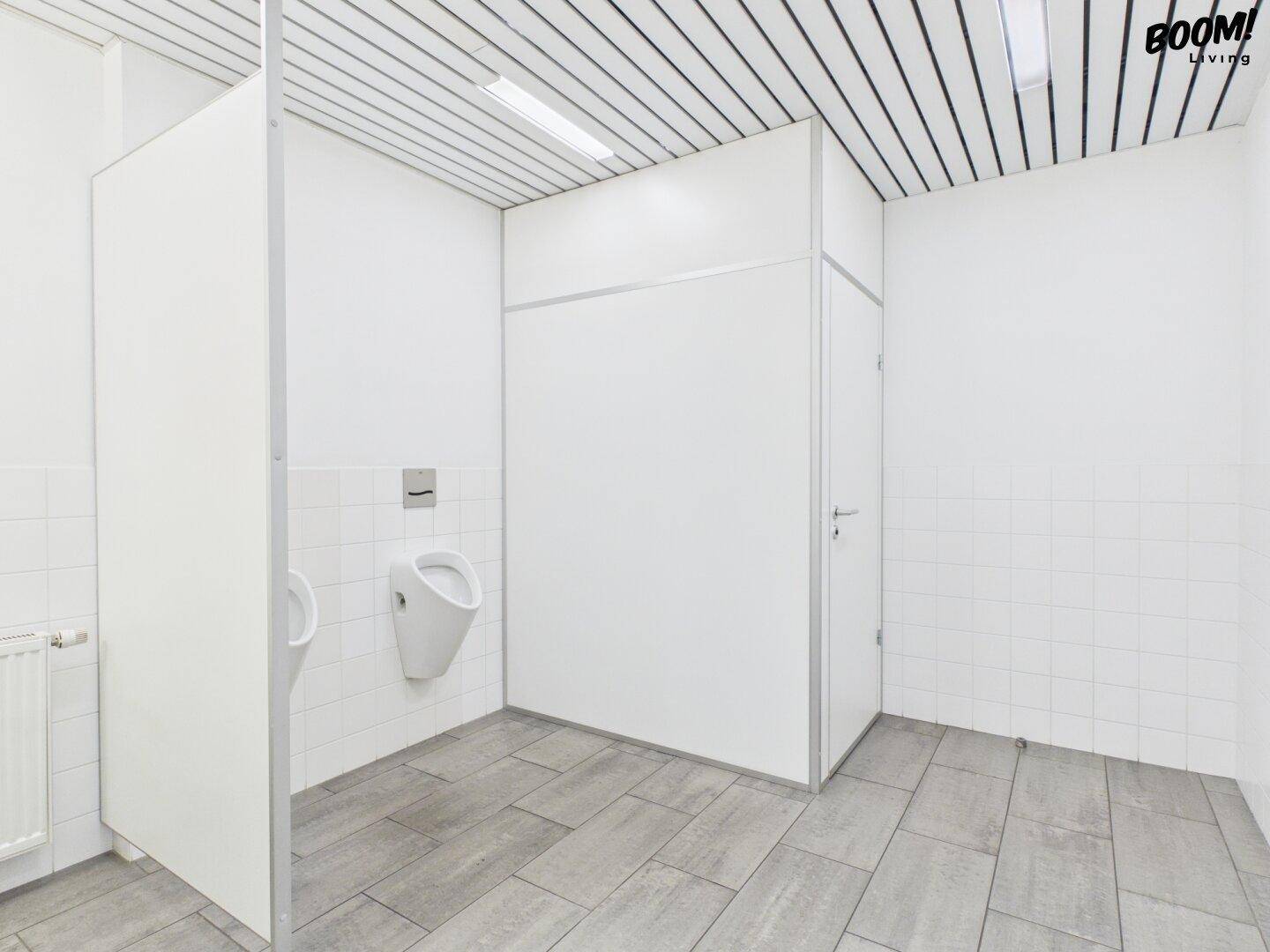 Geräumiger Herrenwaschraum mit Urinalen, gefliestem Boden und weißen Trennwänden, sehr funktional.