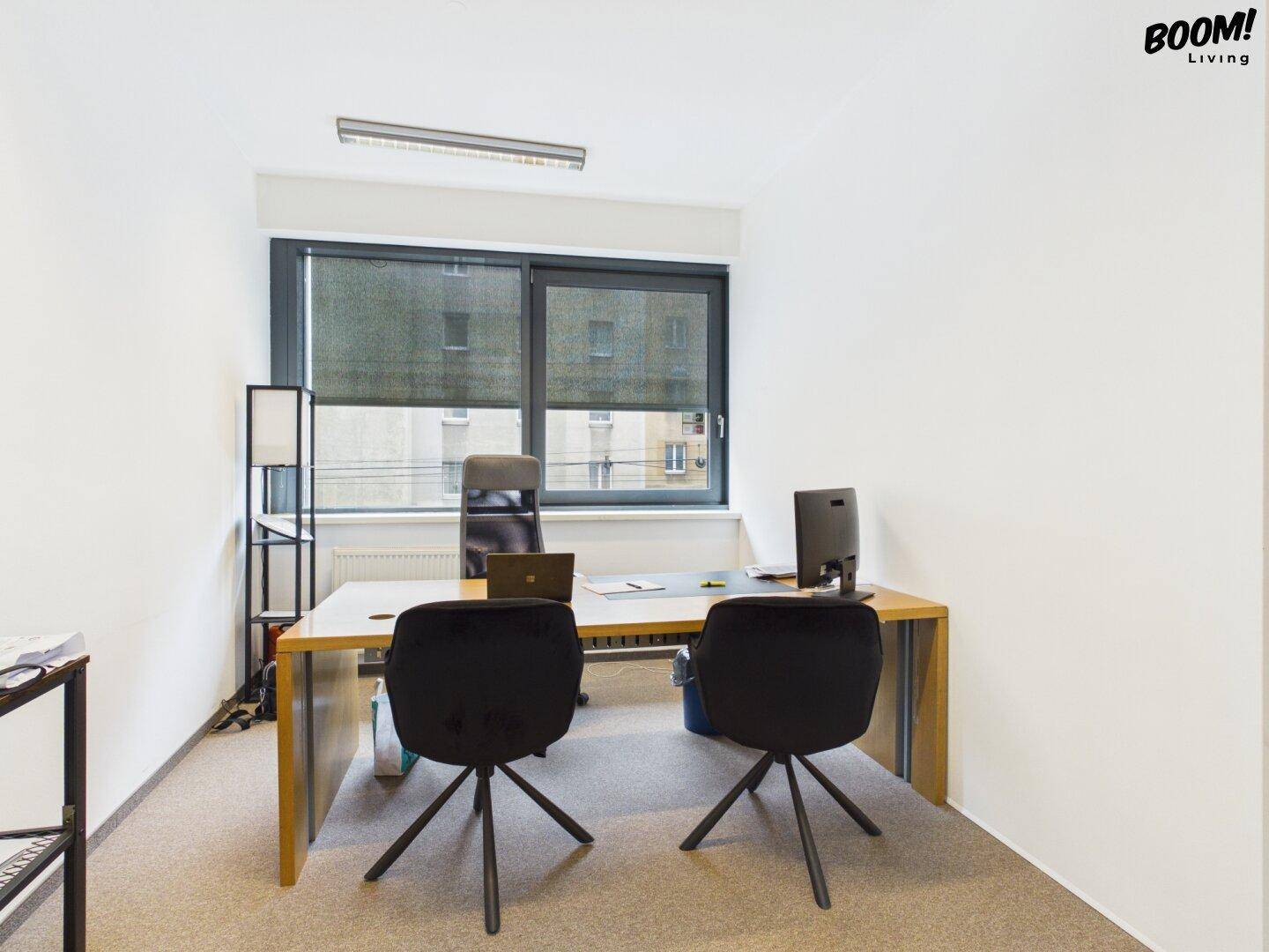 Schlichtes Büro mit zwei Arbeitsplätzen, großen Fenstern und Teppichboden, ideal für konzentriertes Arbeiten.