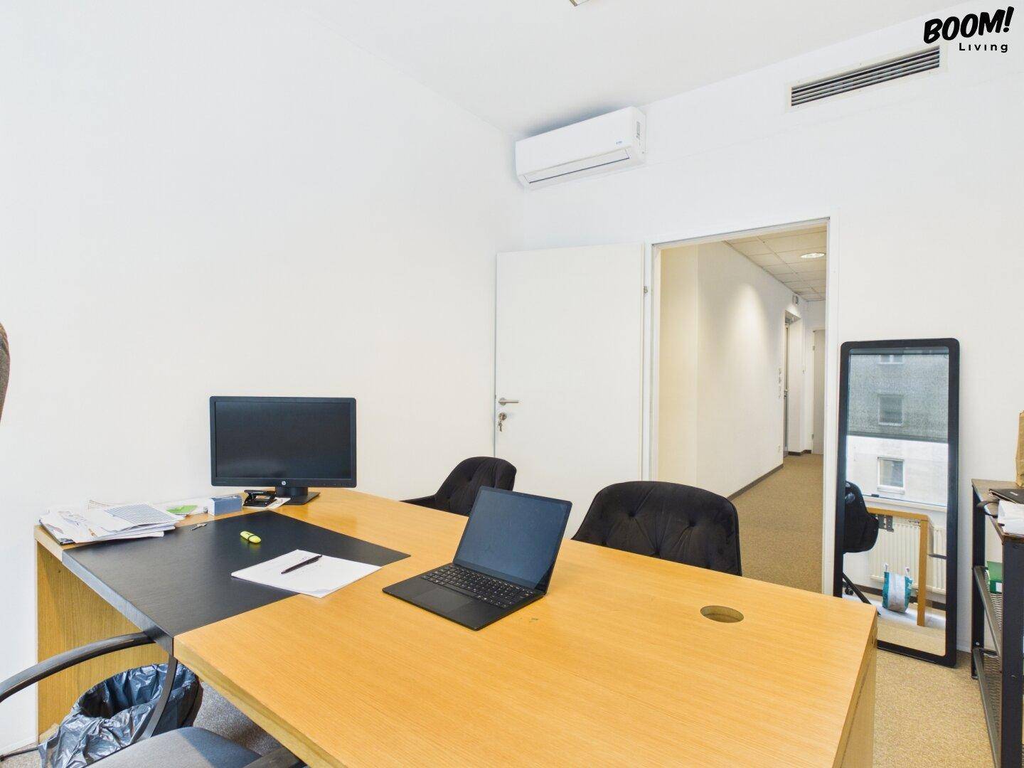 Helles Büro mit Holzschreibtisch, Laptop und Bürostühlen, mit Blick in den Flur.