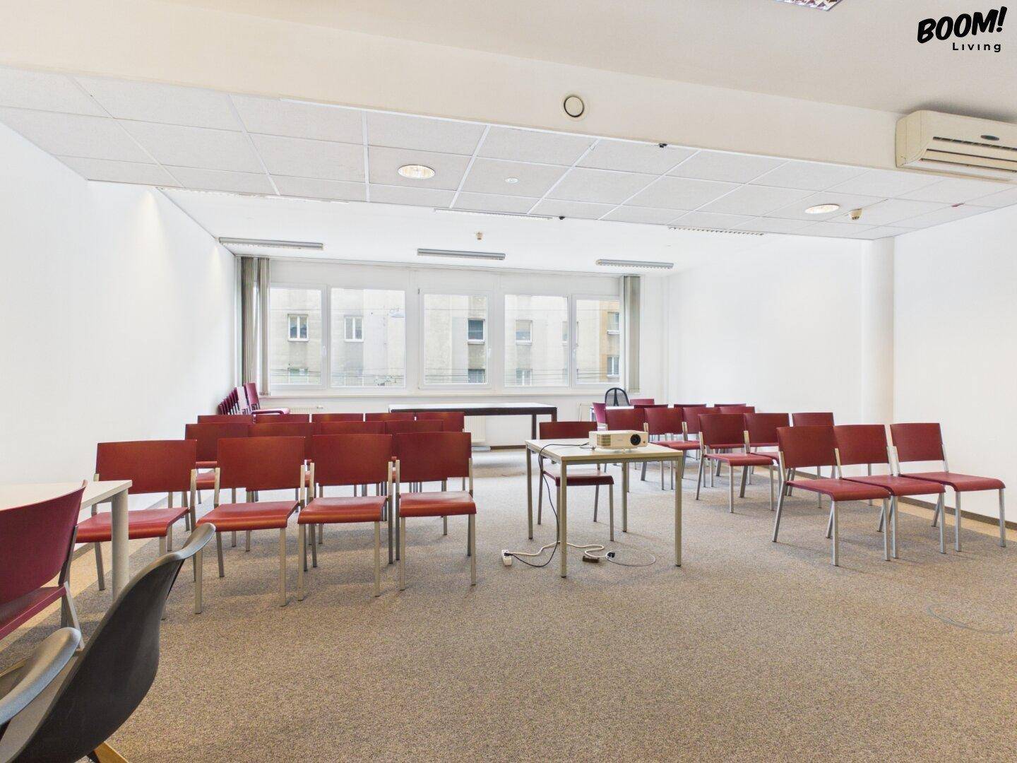 Geräumiger Konferenzraum mit Reihen von roten Stühlen und einem Projektor, ideal für Präsentationen.