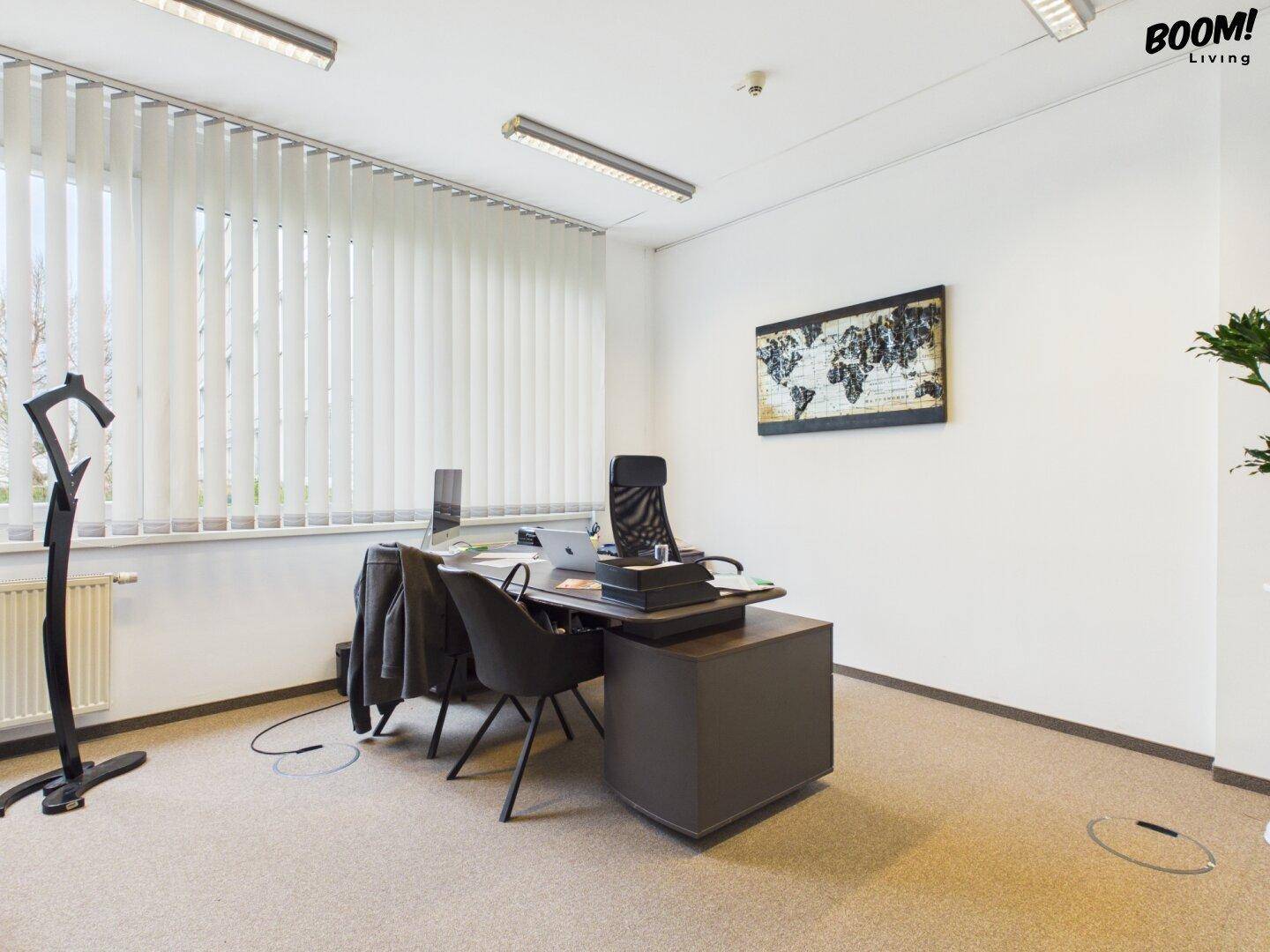 Geräumiges Büro mit mehreren Arbeitsplätzen, vertikalen Jalousien und einem Weltkartenbild an der Wand.