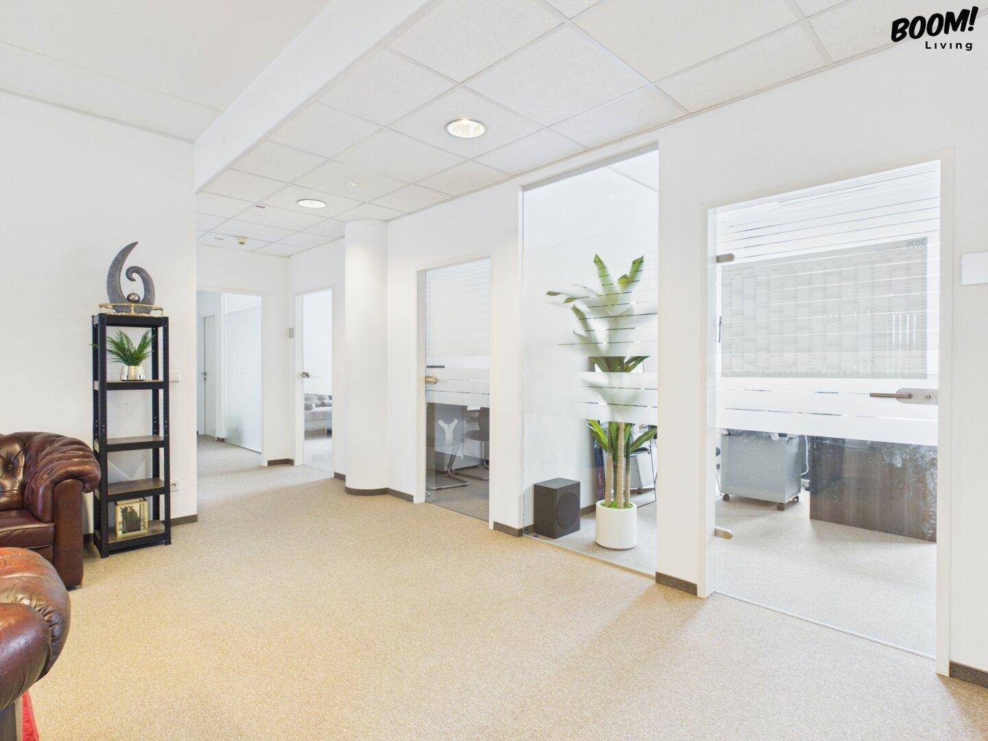 Einladender Empfangsbereich mit Ledersofa, Teppichboden und Blick auf weitere Büroräume.