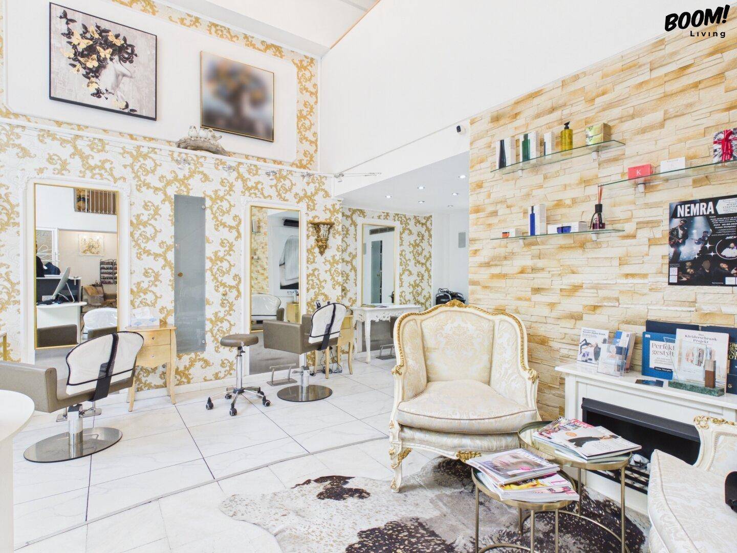 Geräumiger Schönheitssalon mit hohen Decken, goldener Tapete, weißen Fliesen und mehreren Frisierplätzen.