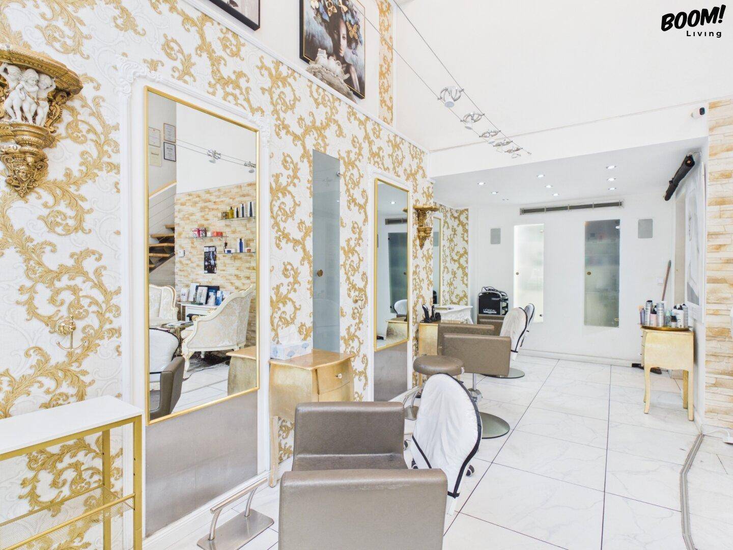 Innenansicht des Schönheitssalons mit eleganten Spiegeln, goldener Tapete und modernen Frisierstühlen.