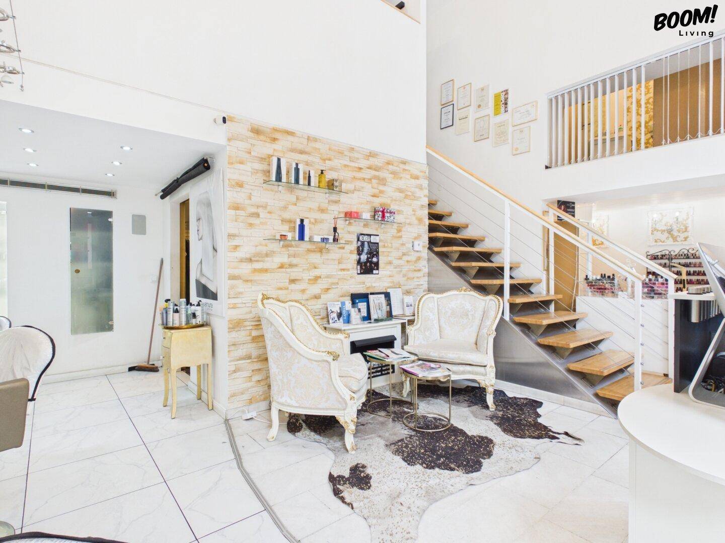 Empfangsbereich mit Steinwand, eleganten Sesseln und einer offenen Holztreppe, die in die obere Etage führt.