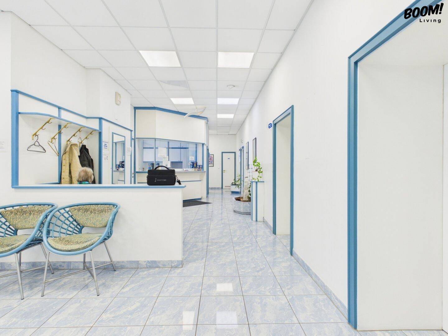 Heller Flur mit Rezeption und Garderobe, blauen Akzenten und Fliesenboden, führt zu weiteren Räumen.