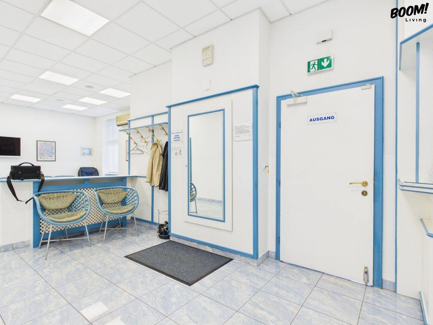 Empfangsbereich mit Garderobe, Spiegel und Ausgangstür, helle Wände und Fliesenboden.