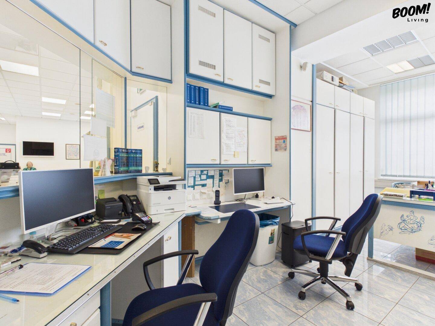 Büroarbeitsplatz mit Computern, Schreibtischen und blauen Bürostühlen, integriert in die Praxisräume.