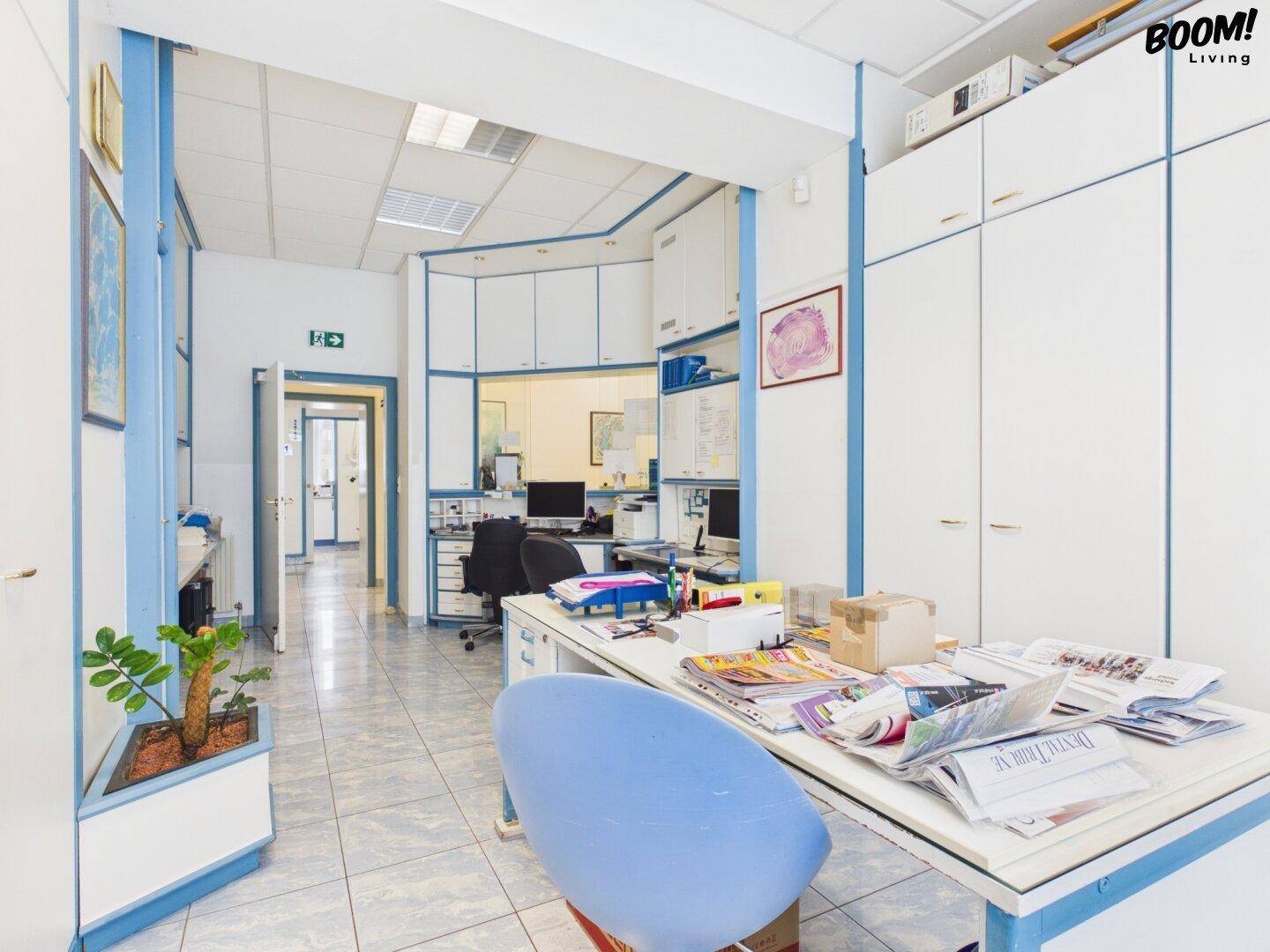 Büro mit Schränken und Arbeitsplatz, helle Wände und Fliesenboden, gut organisiert.