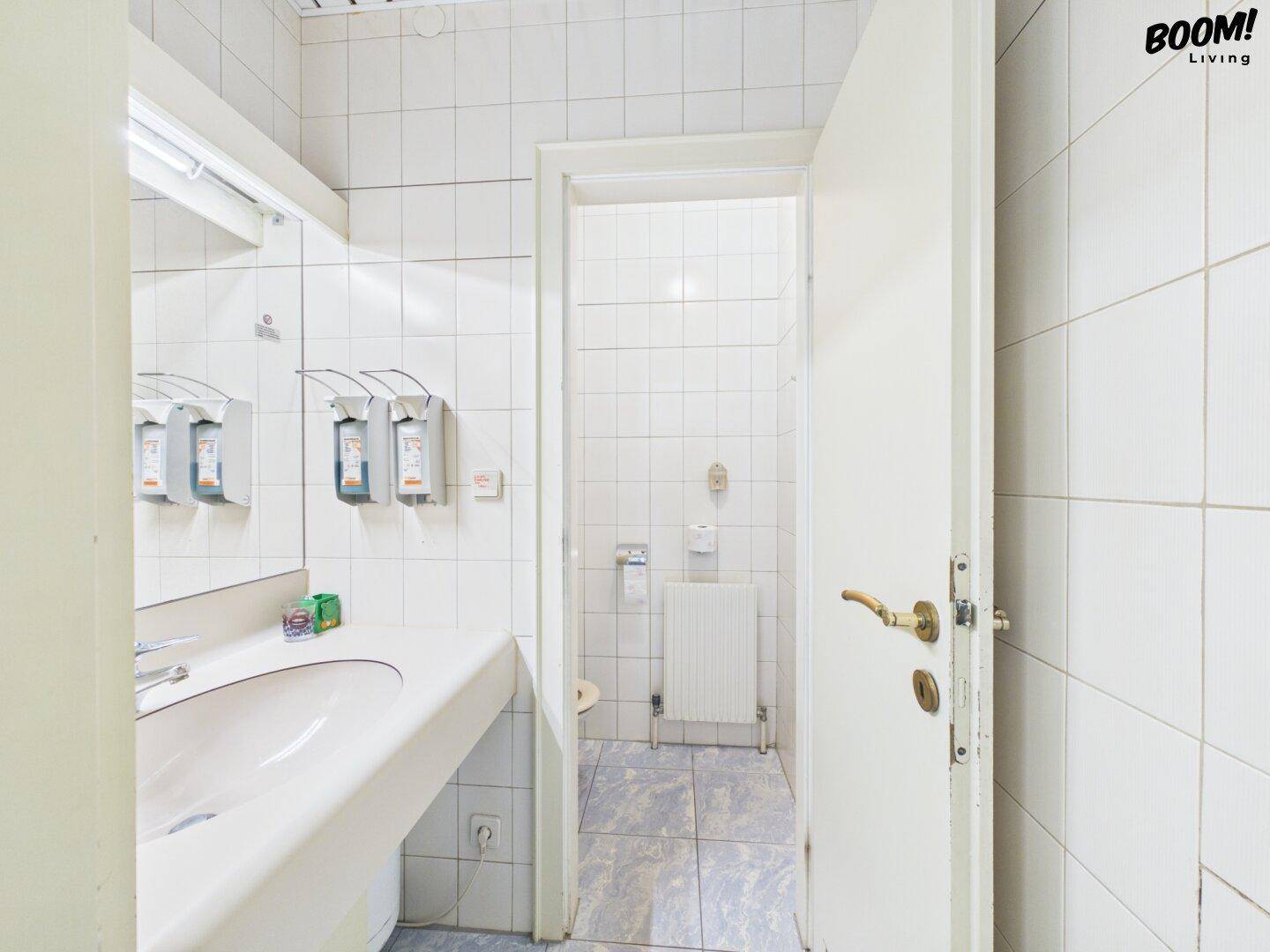 Badezimmer mit Waschbecken, Spiegel und Zugang zur Toilette, komplett gefliest.