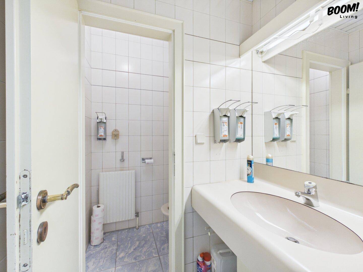 Badezimmer mit Waschbecken, Spiegel und Zugang zur Toilette, komplett gefliest.