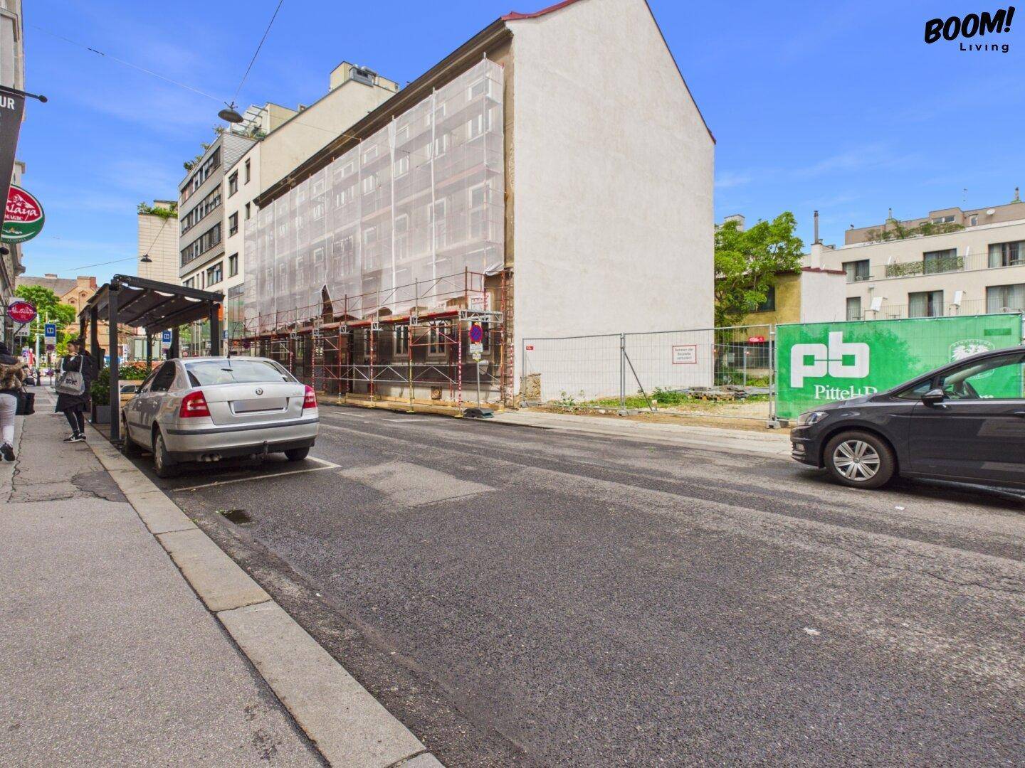 Straßenansicht eines Gebäudes unter Renovierung mit Gerüst und angrenzender Baustelle.