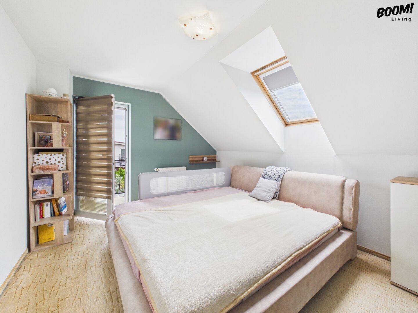 Gemütliches Schlafzimmer im Dachgeschoss mit Dachfenster und Zugang zu einem kleinen Balkon.