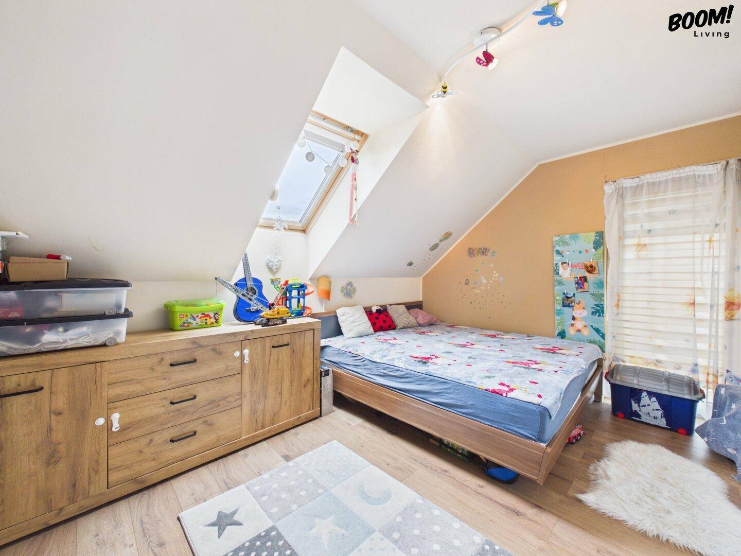 Helles Kinderzimmer im Dachgeschoss mit Dachfenster, Holzboden und bunter Dekoration.