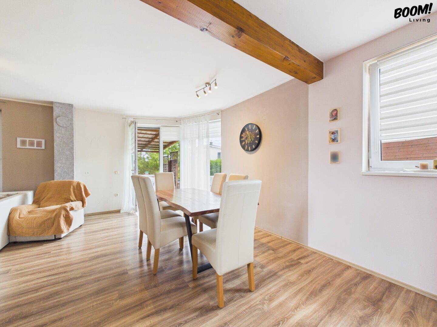 Essbereich mit Holztisch und weißen Stühlen, verbunden mit dem Wohnzimmer und Terrassenzugang.