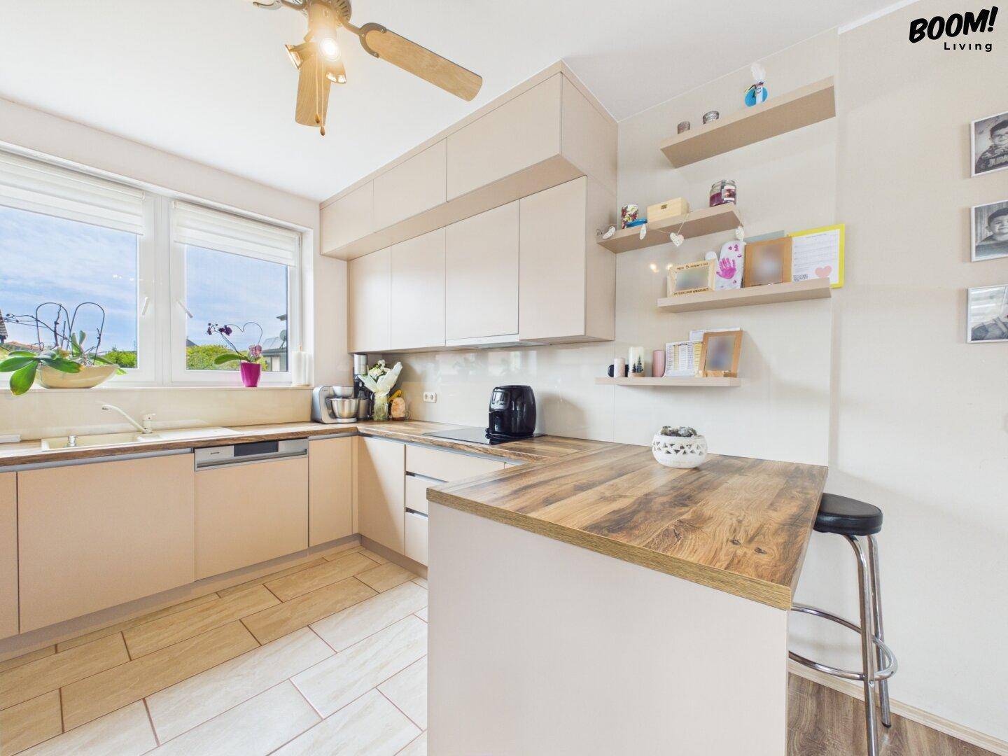 Moderne Küche mit beigen Schränken, Holzarbeitsplatte, Kücheninsel und Fenster.