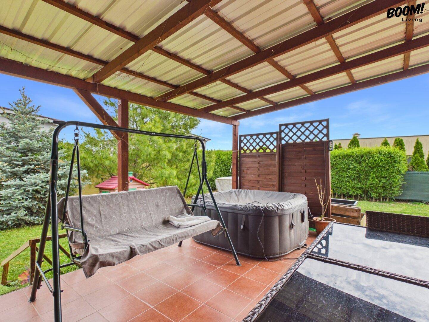 Überdachte Terrasse mit Schaukel, Whirlpool und Blick auf den Garten.