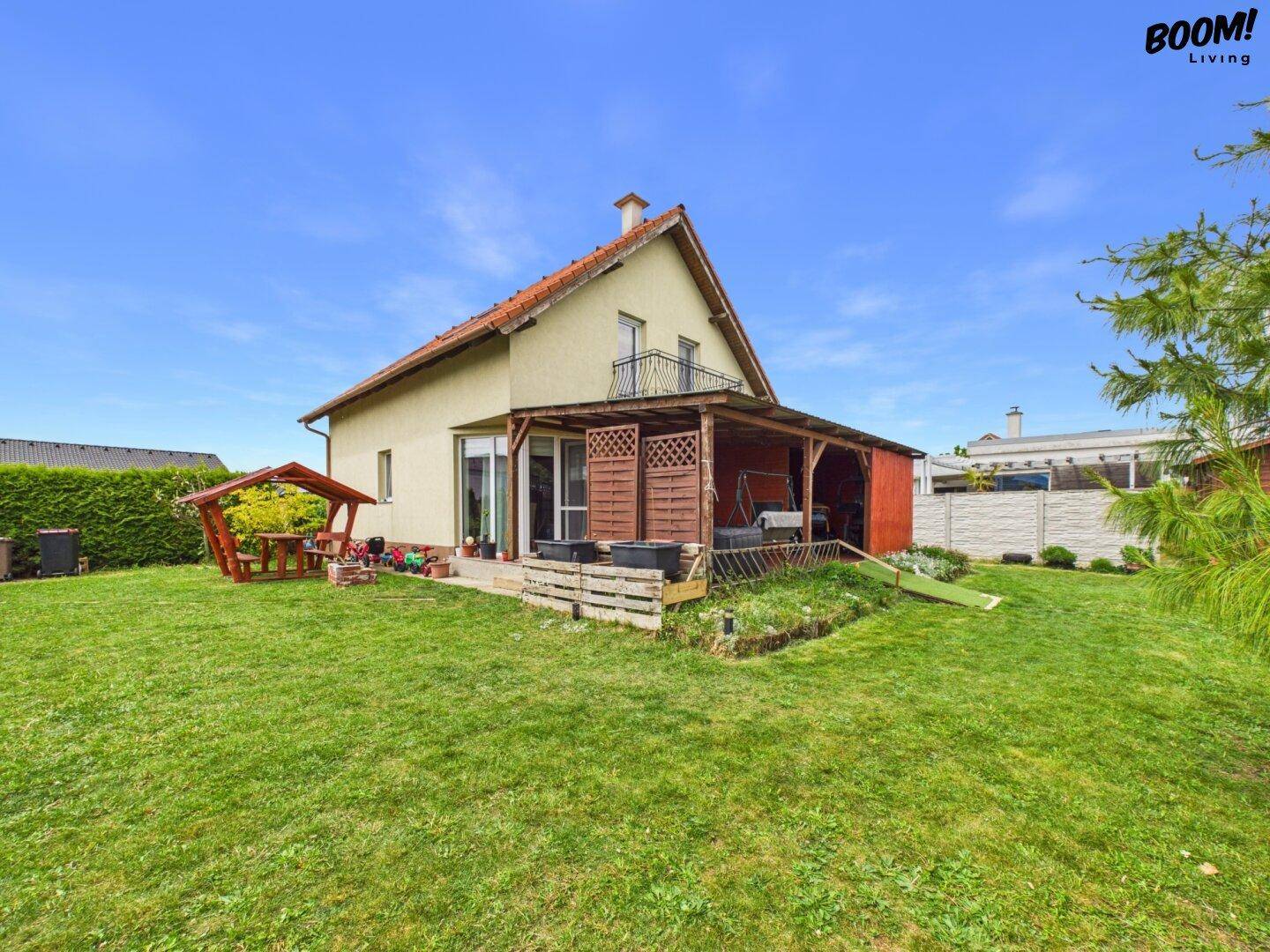 Weitläufiger Garten mit Rasen, überdachter Terrasse und Blick auf das Haus.
