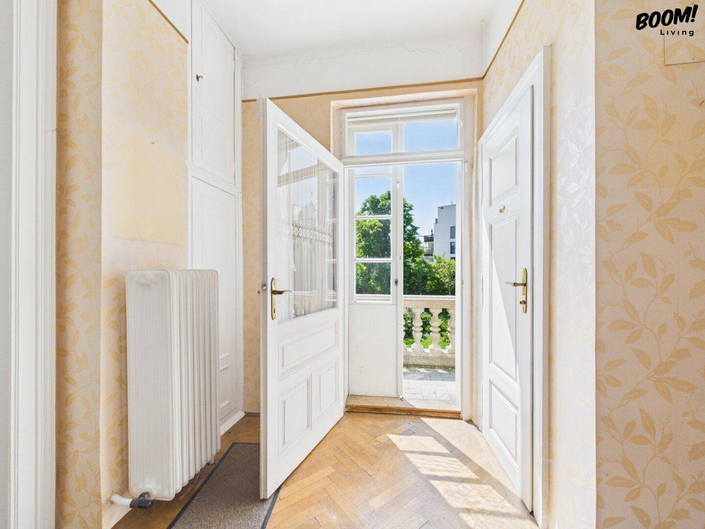 Heller Flur mit Fischgrätparkett, floraler Tapete und Zugang zu einem französischen Balkon.