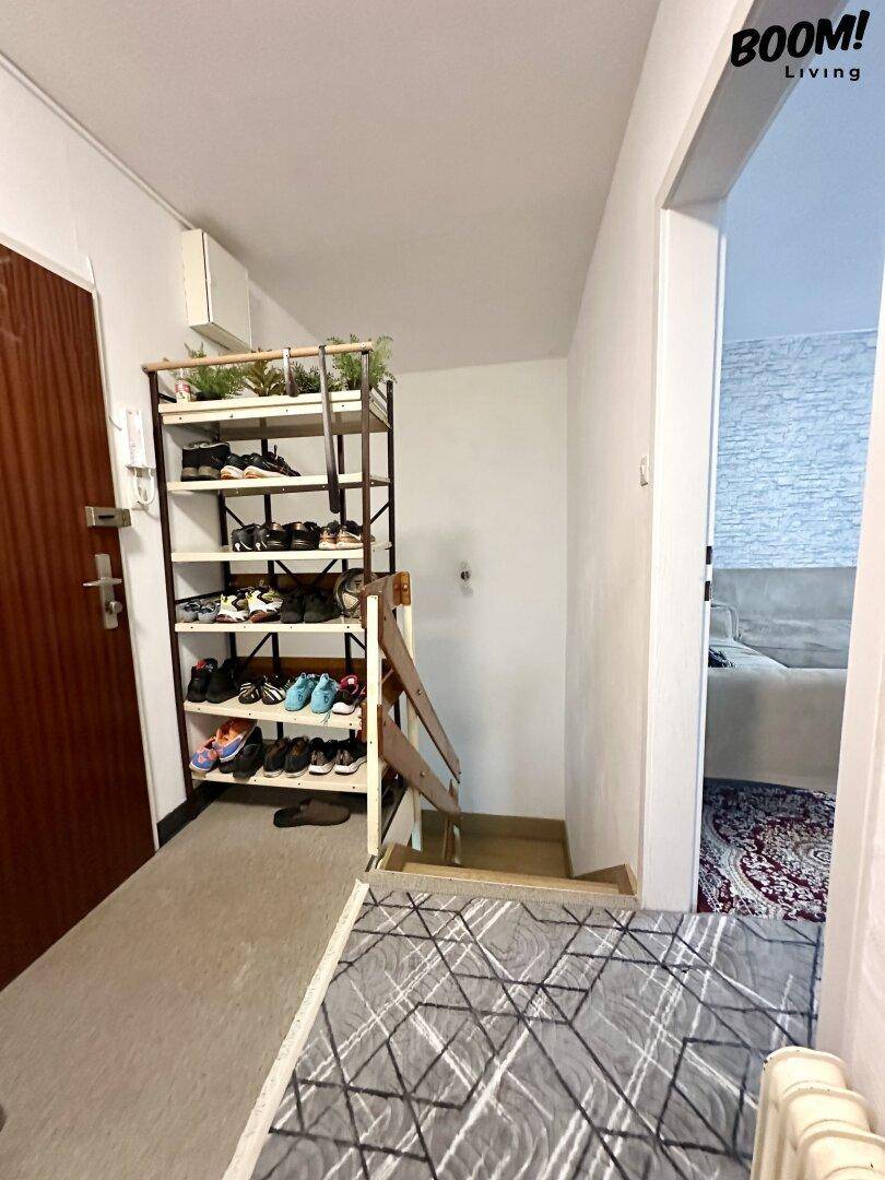 Heller Flur mit Schuhregal und Treppe, die in eine untere Etage führt.