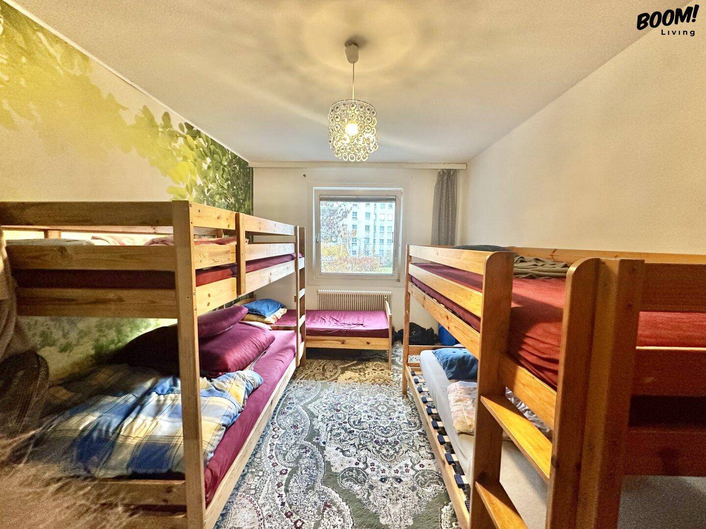 Kinderzimmer mit mehreren Etagenbetten, Teppichboden und einer farbigen Wandgestaltung.