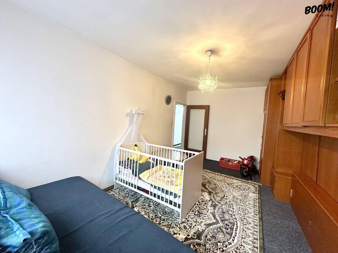 Schlafzimmer mit Babybett, Schlafsofa und großem Einbauschrank an der Wand.