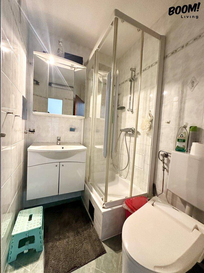 Kleines Badezimmer mit Duschkabine, WC, Waschbecken und hellen Fliesen.
