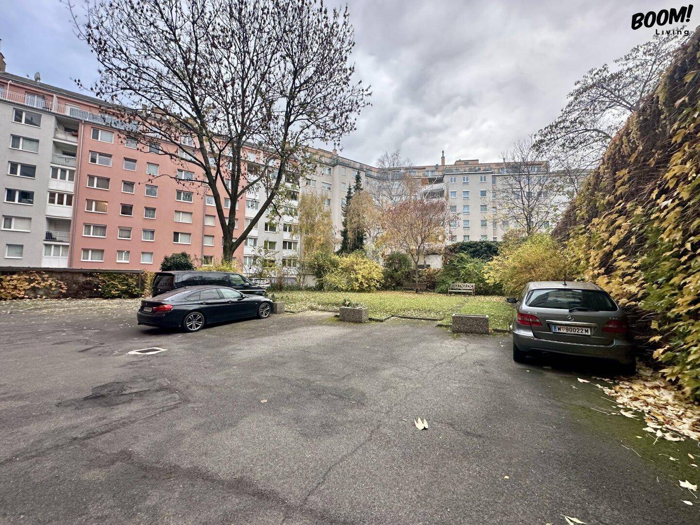 Blick auf den Innenhof mit Parkplätzen und umliegenden Wohngebäuden unter bewölktem Himmel.