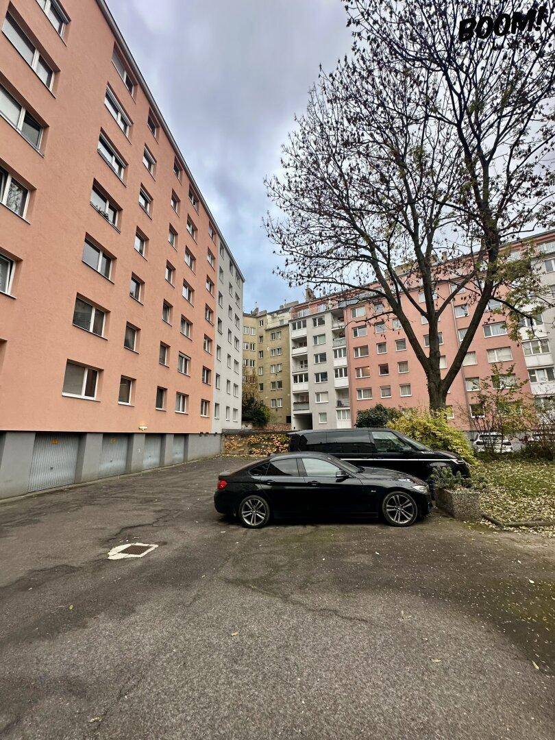 Außenansicht des Wohngebäudes mit Parkplätzen und mehreren Stockwerken unter bewölktem Himmel.