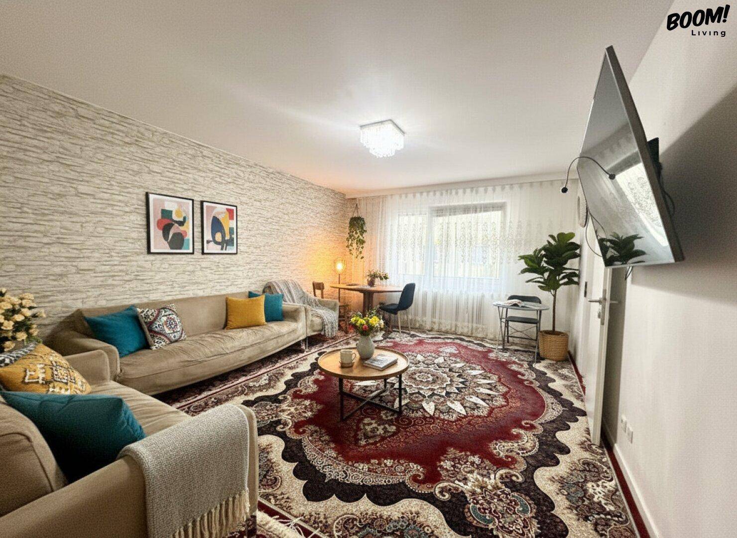 Gemütliches Wohnzimmer mit großem Orientteppich, bequemer Couch und kleinem Essbereich am Fenster.