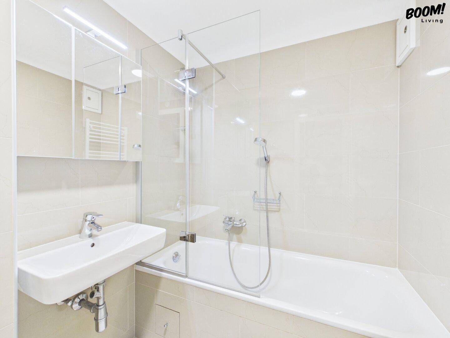 Modernes Badezimmer mit beigen Fliesen, Badewanne mit Duschwand und einem einzelnen Waschbecken.