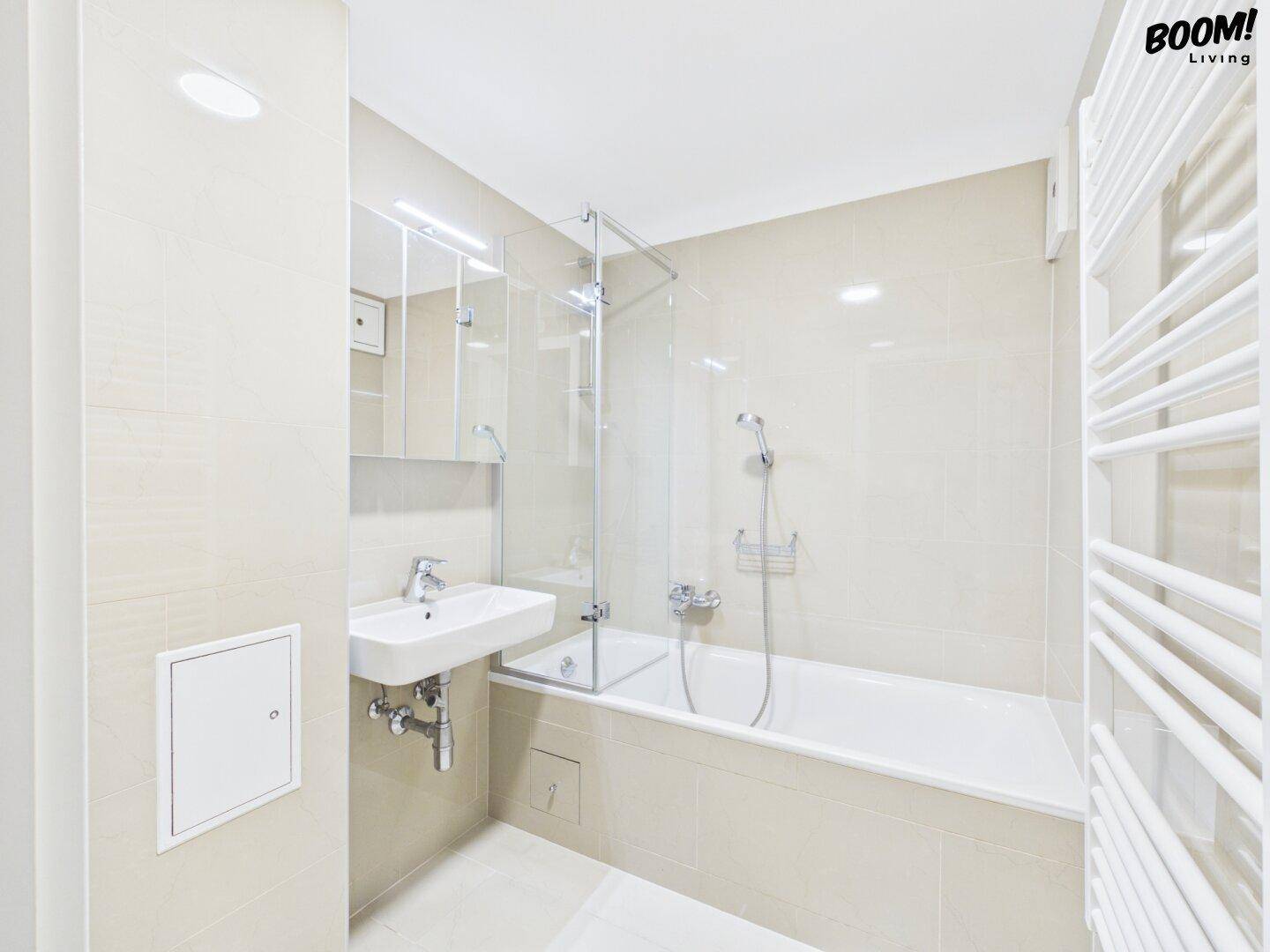 Helles Badezimmer mit beigen Fliesen, Badewanne mit Duschabtrennung und beheiztem Handtuchhalter.