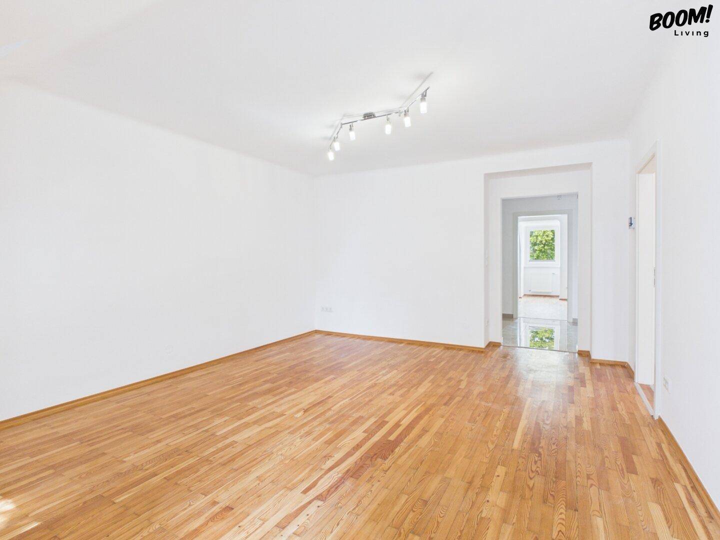 Geräumiger, leerer Raum mit Parkettboden und offenem Zugang zu einem weiteren hellen Zimmer.