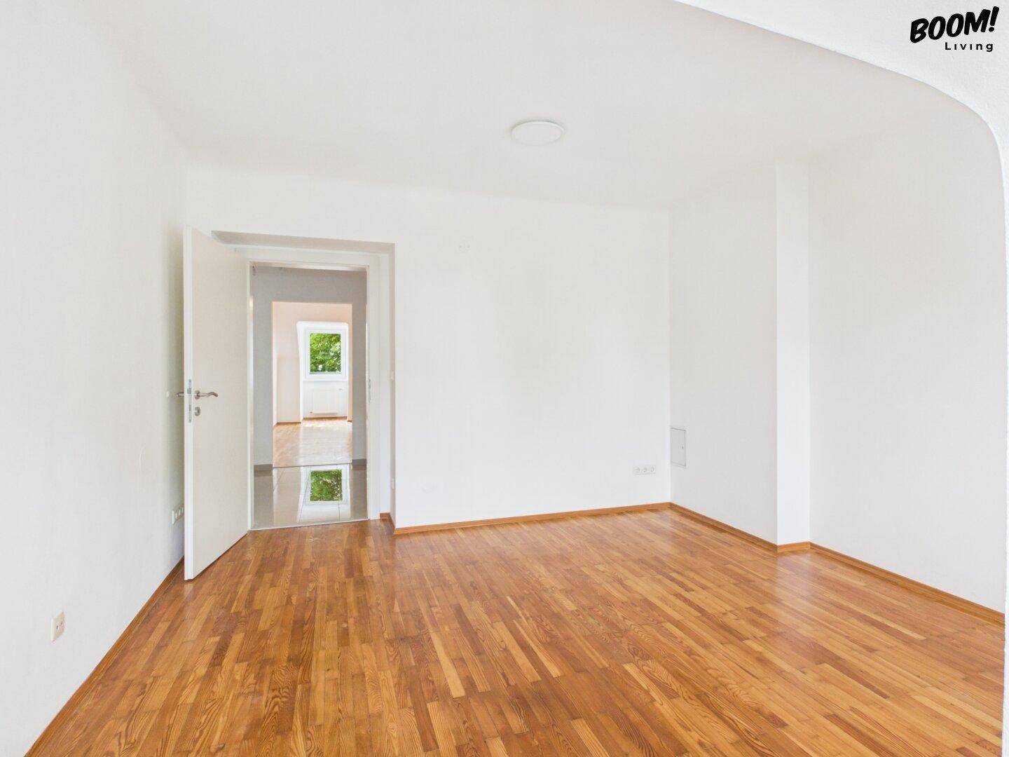 Geräumiger, heller Raum mit Parkettboden und offenem Zugang zu einem weiteren Zimmer mit Tageslicht.